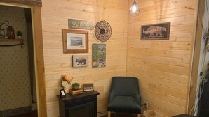 Een gezellige kamer met houten wanden, een open haard, een groene stoel en diverse decoraties, waaronder een bord met 'Olympic National Park' en een bord met 'Hibernation Station'.