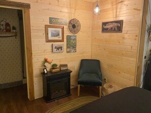 Una habitación acogedora con paredes de madera, una chimenea, un sillón verde y varias decoraciones en las paredes, incluyendo un cartel de 'Olympic National Park' y un letrero de 'Hibernation Station'.
