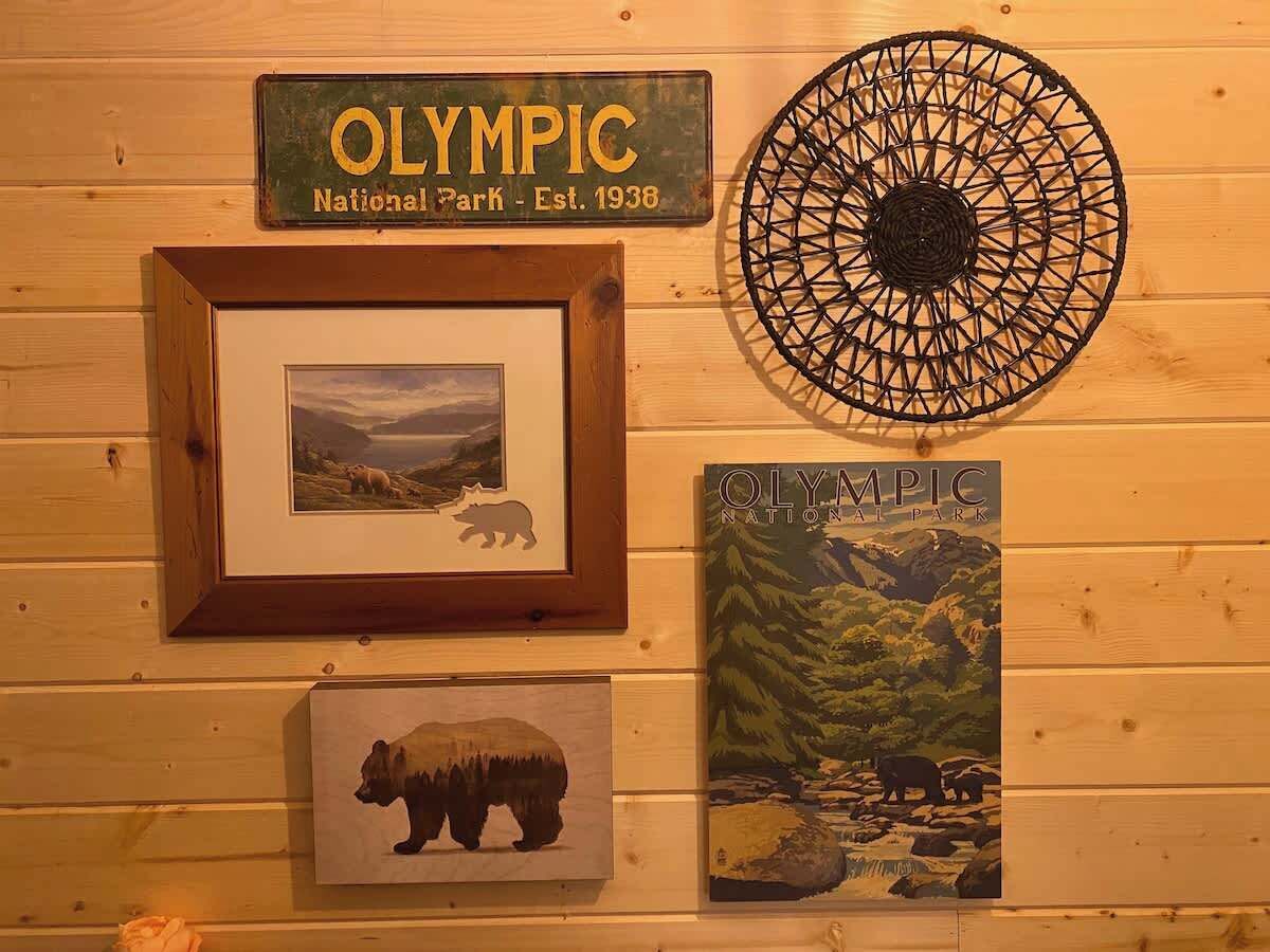 Een houten wand met een lijst met een berenafbeelding, een lijst met een bord van Olympic National Park, een rond geweven object en een poster van een beer en een landschap.