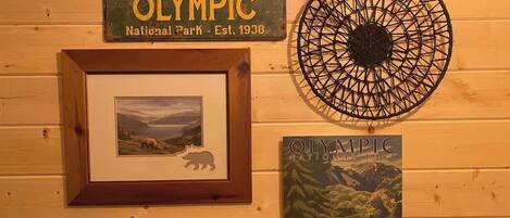 Een houten wand met een lijst met een berenafbeelding, een lijst met een bord van Olympic National Park, een rond geweven object en een poster van een beer en een landschap.