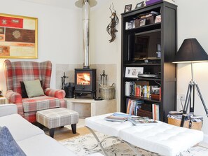 A cozy living room with a fireplace, a plaid armchair, a bookshelf, and a lamp.