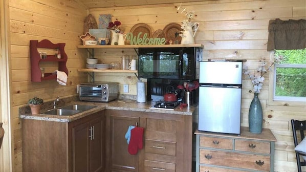 A wooden cabin kitchen with a microwave, toaster, sink, and a refrigerator.