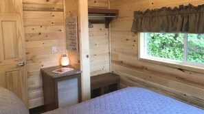 A small, cozy room with wooden walls, a window with a view of greenery, a sink, and a bed. - Cedar Heights Cabin Olympic Strait View (Port Angeles)