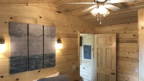 A wooden cabin interior with a ceiling fan, a painting on the wall, and a door.