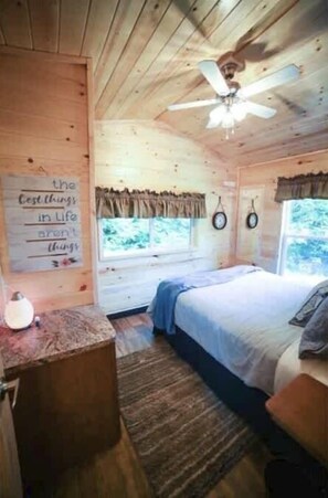 A wooden cabin bedroom with a bed, a ceiling fan, a window, and a wall with a quote. - Cedar Heights Cabin Olympic Strait View (Port Angeles)