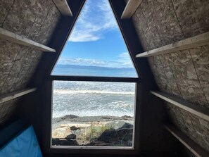A triangular window with a view of the ocean and rocky shoreline. - Whiskey Creek Beach Front A-Frame Site 9 (Port Angeles)