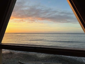 Une vue sur l’océan, prise à travers une fenêtre, avec une côte rocheuse au premier plan.