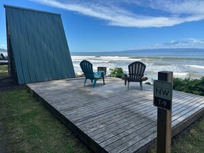Una terraza de madera con dos sillas Adirondack mirando al océano, un cobertizo verde y un letrero que indica NW T-9.