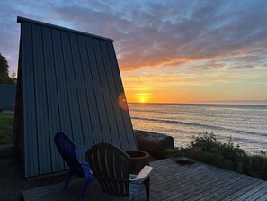 A wooden deck with a metal shed, a chair, and a view of the ocean at sunset.