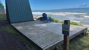 Eine Holzterrasse mit einem blauen Stuhl und einer grünen Struktur mit Blick auf einen Strand und Wellen.