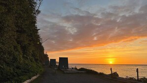 Ein Kiesweg führt zu einem Strand mit Sonnenuntergang, einem Zaun und einigen Gebäuden.