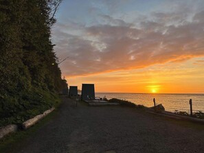 Ein Kiesweg führt zu einem Strand mit Sonnenuntergang, einem Zaun und einigen Gebäuden.