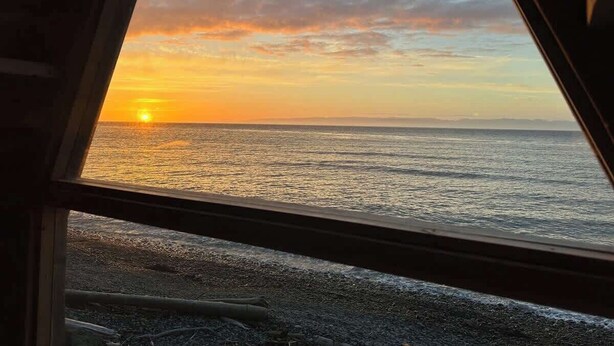 A sunset view from a window overlooking a beach with the ocean and a distant horizon. - Whiskey Creek Beach Front A-Frame Site 11 (Port Angeles)
