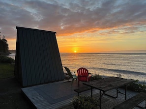 Vista do pôr do sol a partir de um deck de madeira com estrutura metálica, duas cadeiras e uma mesa.