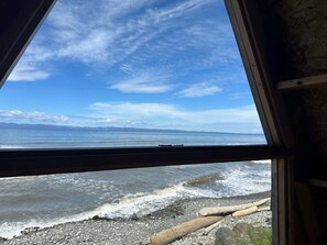A view from a window overlooking a rocky shoreline with waves crashing onto the beach.