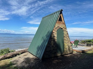 A small, triangular wooden structure with a green roof, located near a body of water.