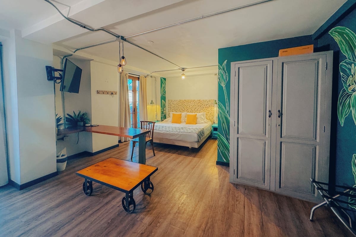 Une chambre avec un plancher en bois, un lit avec des oreillers jaunes, un bureau avec une chaise et une armoire.