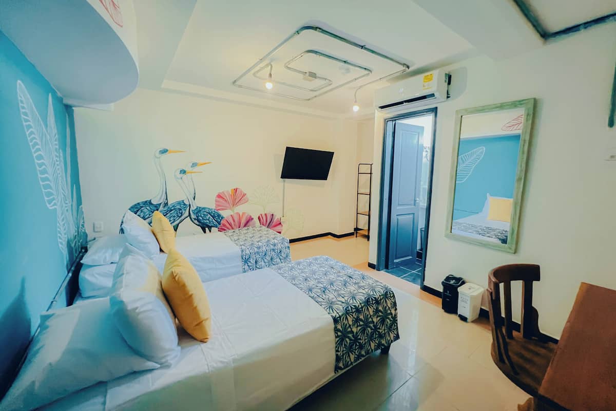 Une chambre d’hôtel avec deux lits, un téléviseur à écran plat, une porte, une chaise et un mur orné d’un tableau.