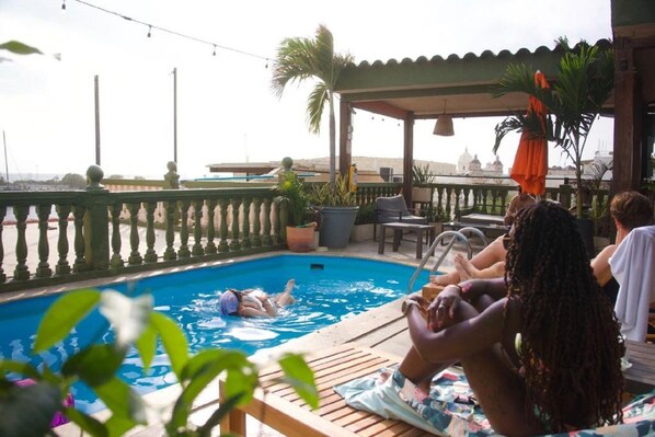 A pool area with a wooden deck, lounge chairs, and potted plants.