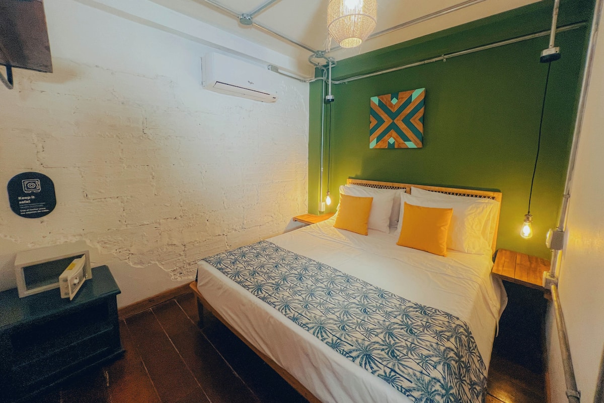 Une chambre à coucher comprenant un lit, une table de chevet, un climatiseur fixé au mur, un élément décoratif mural et un luminaire suspendu.