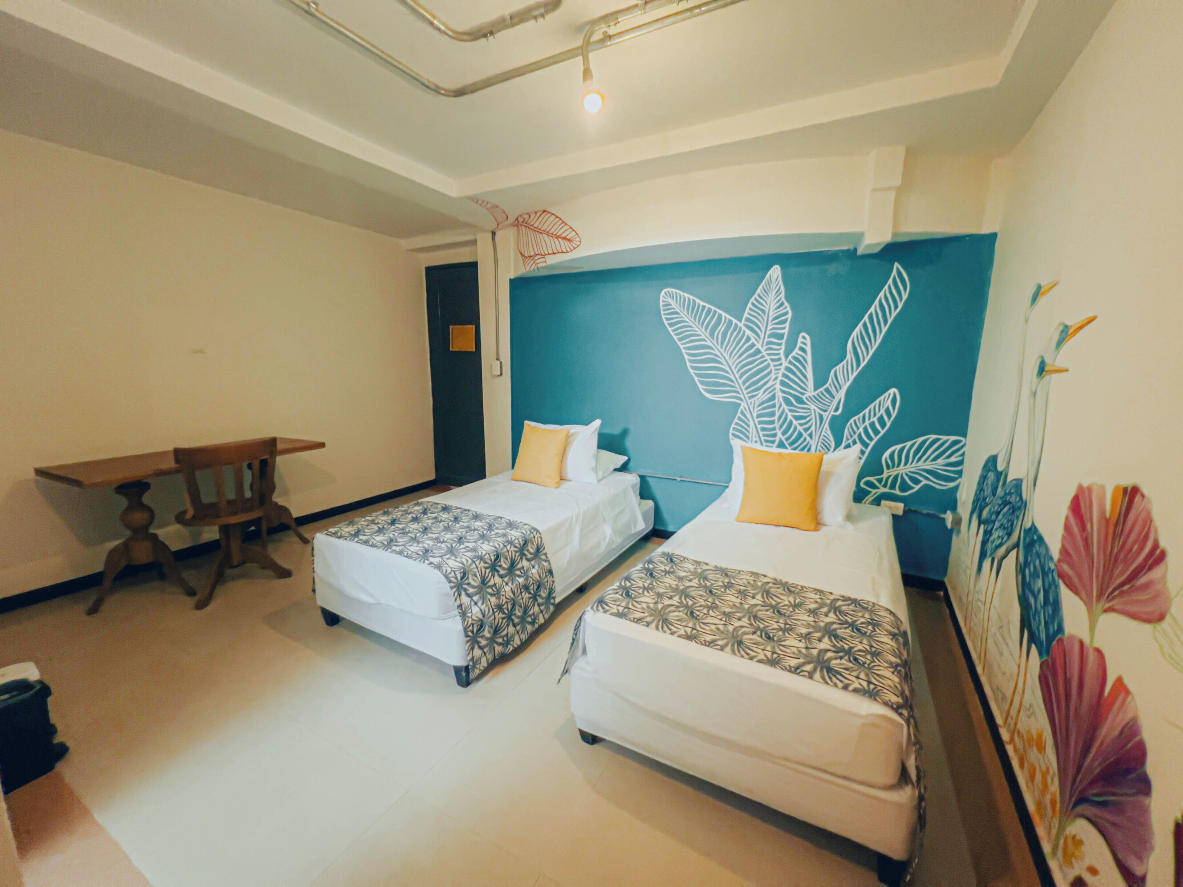 A room with two beds, a wooden table, and a wall with a leaf pattern.