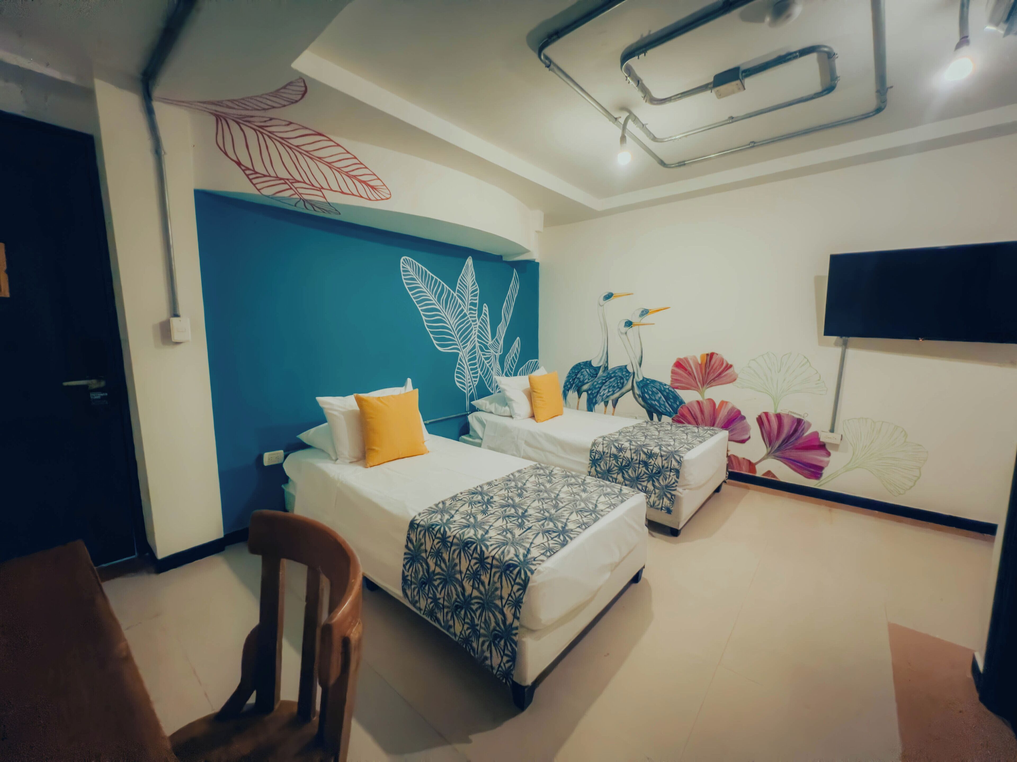 Une chambre d’hôtel avec deux lits, un mur d’accent bleu et une fresque représentant des oiseaux et des fleurs.