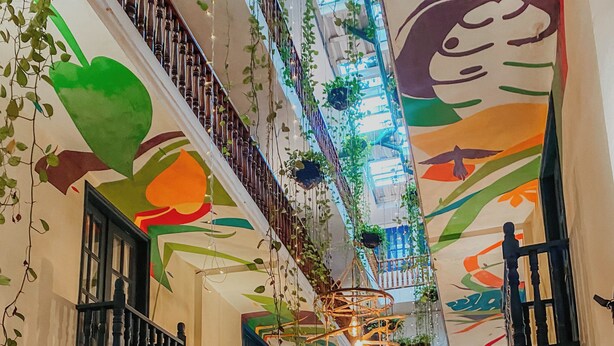 Un espacio interior amplio con techo alto, plantas decorativas y una escalera.