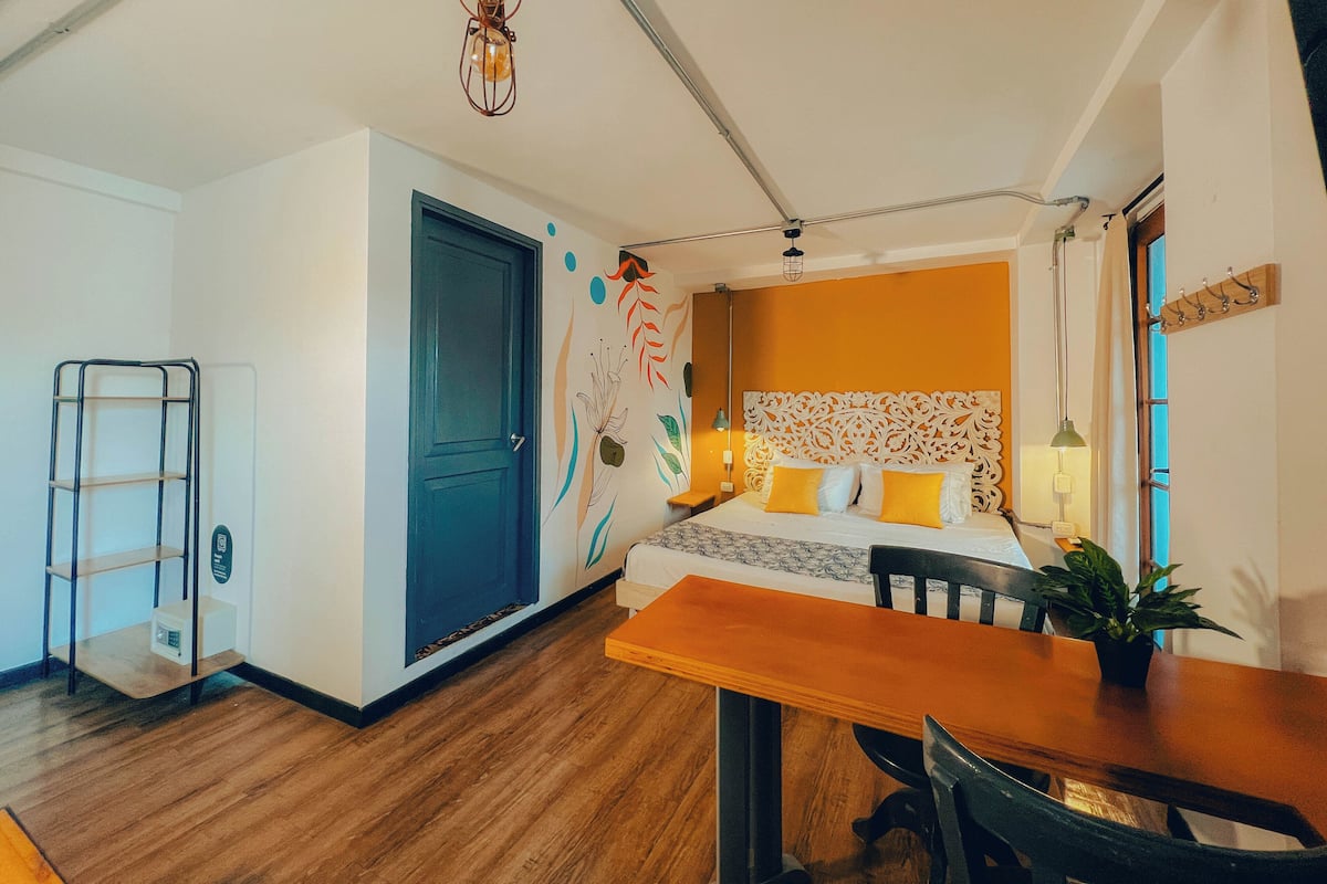 Une petite pièce comprenant un lit, une table en bois, une chaise, un bureau et une petite étagère.