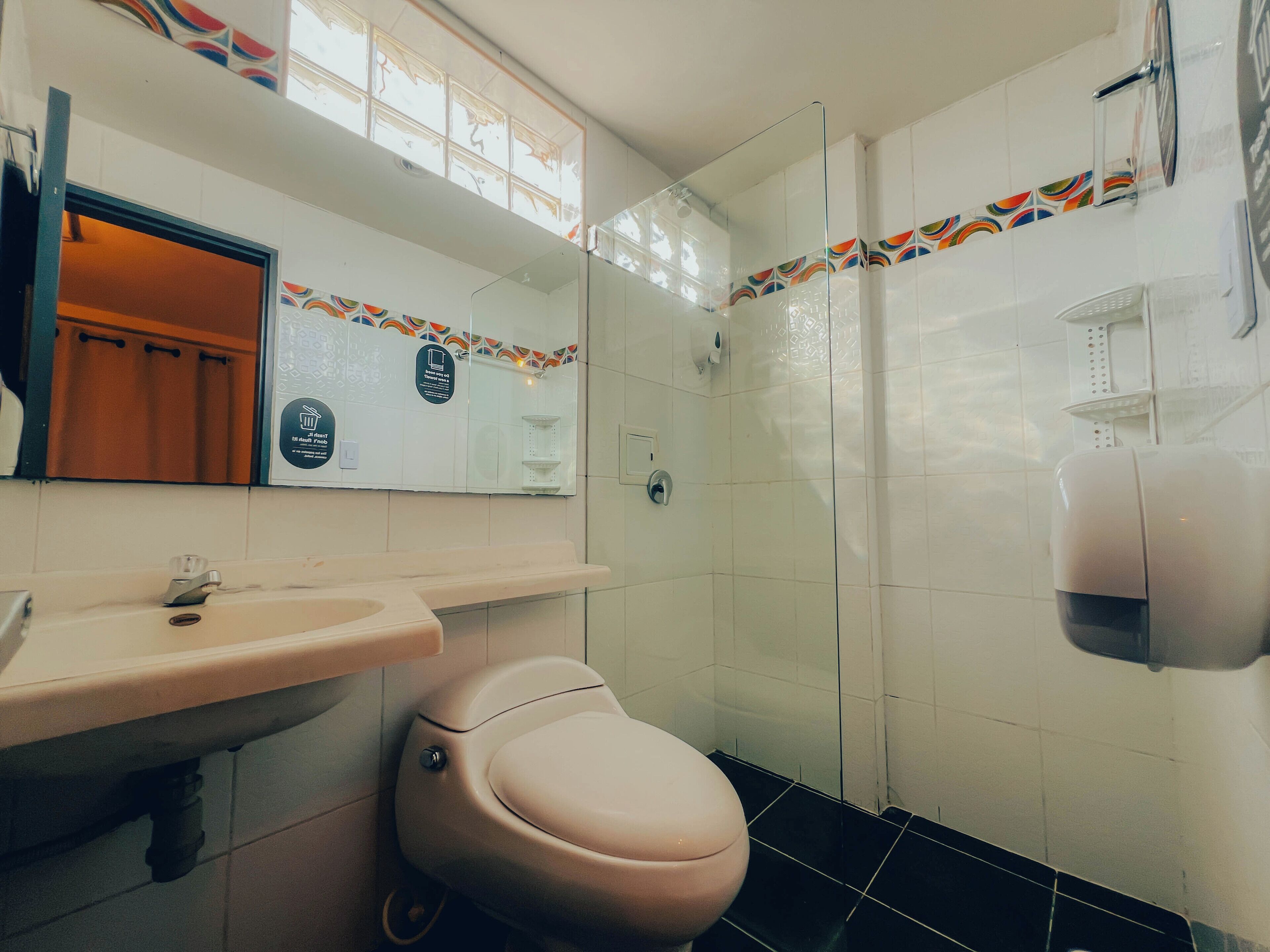 A bathroom with a toilet, sink, mirror, and shower.