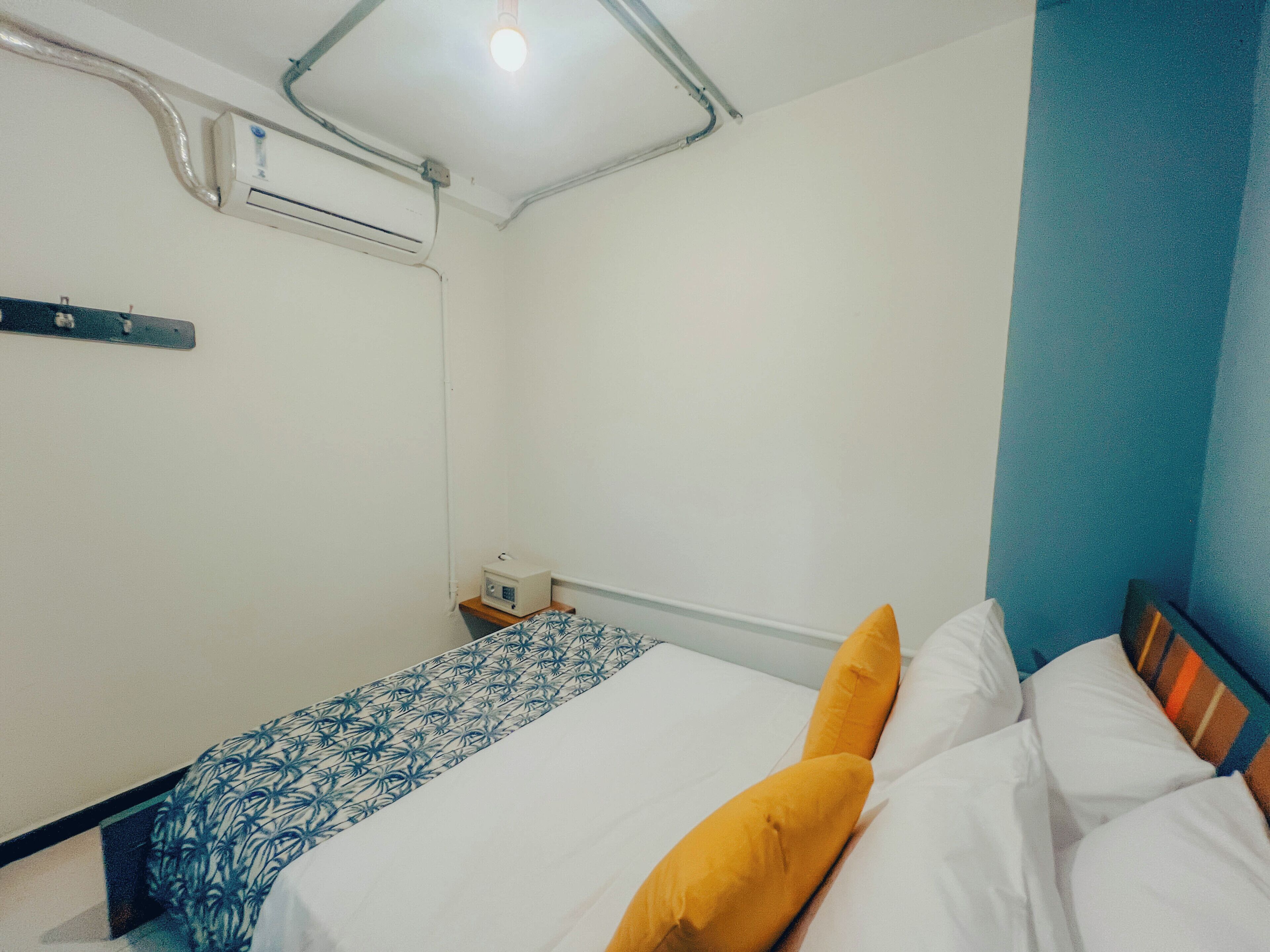 A small, clean room with a bed, a bedside table, and an air conditioning unit on the wall.