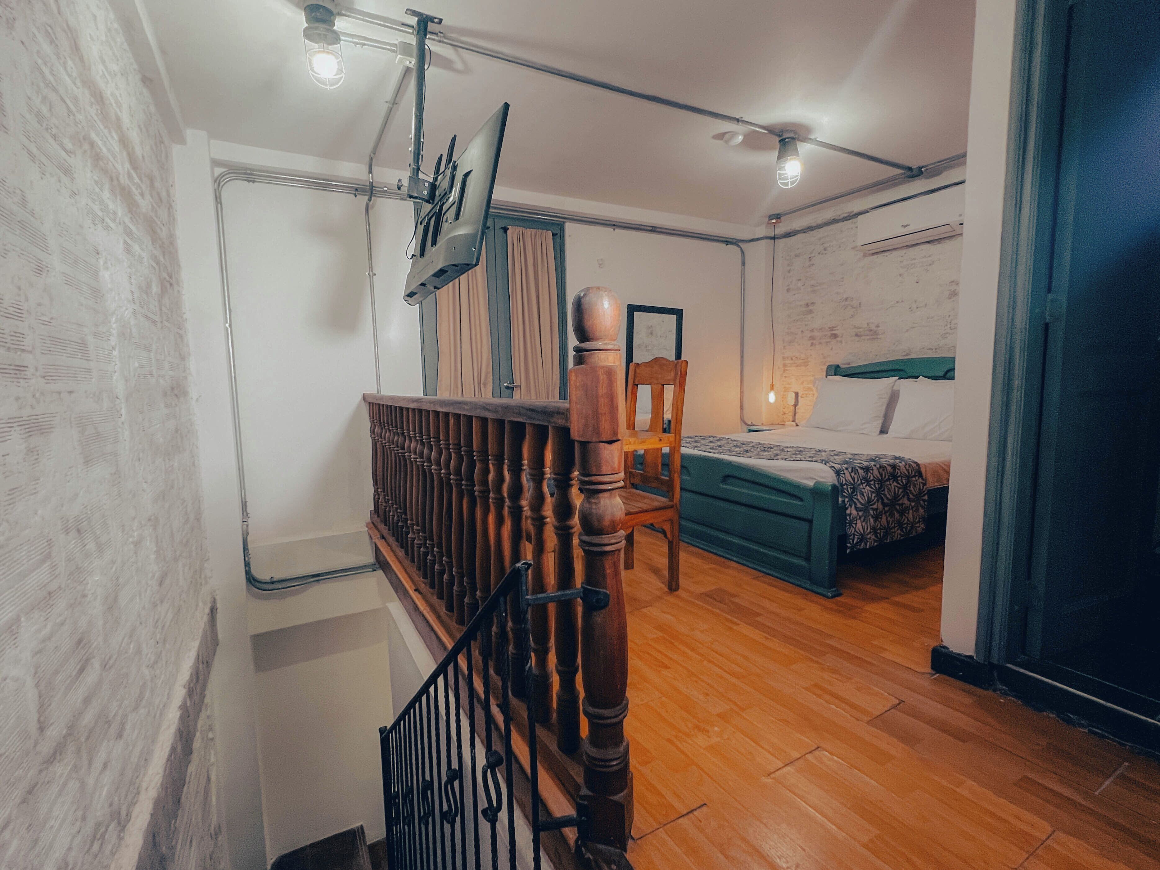 Una habitación con escalera de madera, una cama con colcha estampada, una silla y un ventilador de techo.