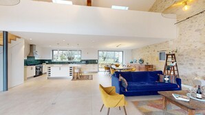 Amplia sala de estar con sofá azul, sillón amarillo y una mesa de comedor con sillas.