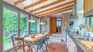A spacious kitchen with large windows, wooden beams, and a stone wall.