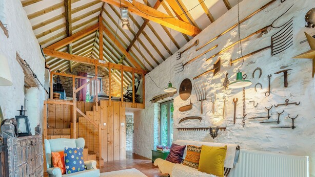 A rustic interior with wooden beams, a loft area, and a collection of tools on the wall.