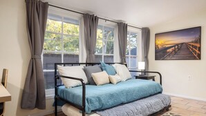 A bedroom with a bed, a nightstand, a window with curtains, and a painting on the wall.