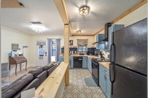 A compact kitchen with a refrigerator, stove, and sink. There is a bench and a dining table with chairs. - Kemp Estate Carriage House | Downtown Ocala 2/1 (Ocala)