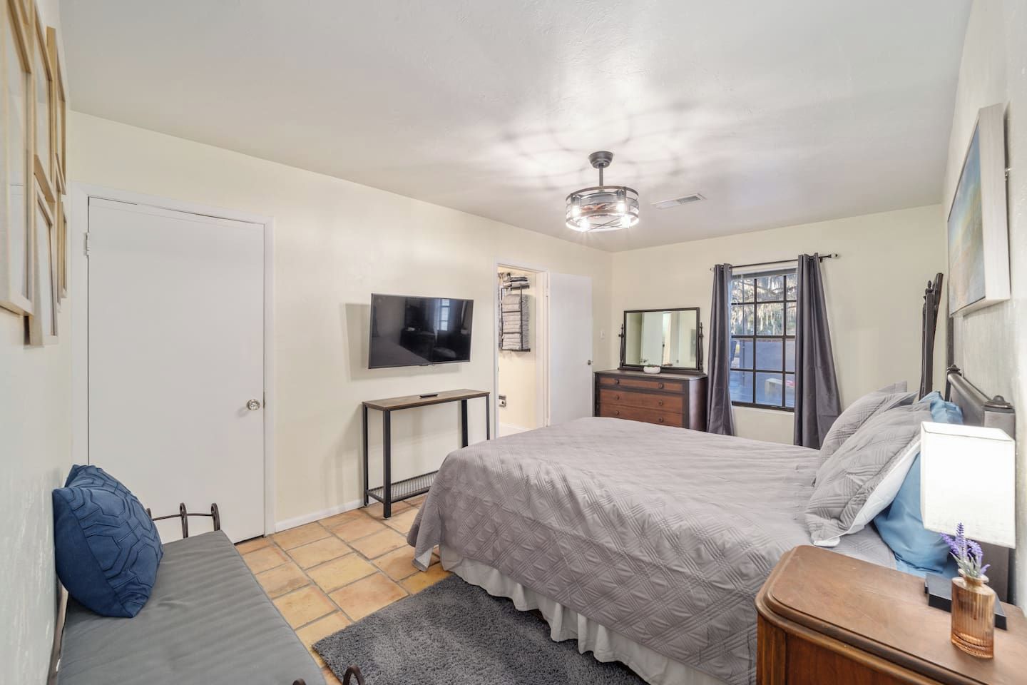 Une chambre à coucher comprenant un lit, une table de chevet, une télévision, une commode et une fenêtre avec des rideaux.