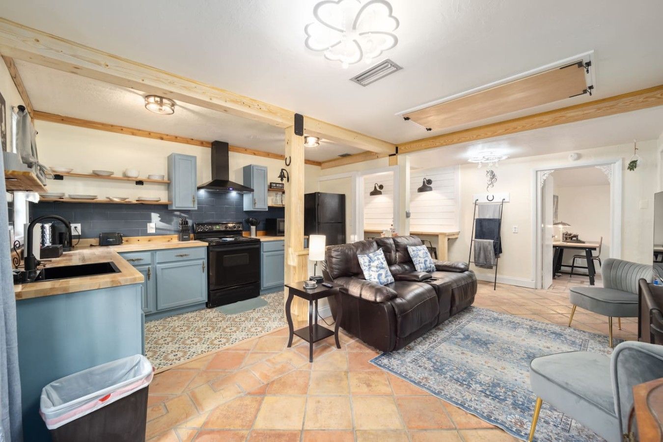 A spacious living area with a leather sofa, a dining table, and a kitchen with blue cabinets and a black stove.