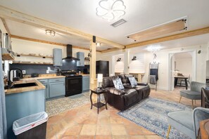 A spacious living area with a leather sofa, a dining table, and a kitchen with blue cabinets and a black stove. - Kemp Estate Carriage House | Downtown Ocala 2/1 (Ocala)