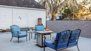 Un patio al aire libre con una mesa y sillas, una chimenea de ladrillo y un edificio blanco al fondo.