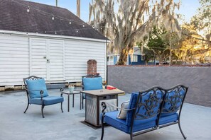Un patio al aire libre con una mesa y sillas, una chimenea de ladrillo y un edificio blanco al fondo.