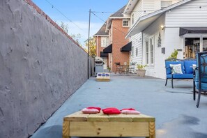 Un estrecho callejón con un banco de madera, una pequeña mesa con cojines, y un edificio con fachada de ladrillo y revestimiento blanco.