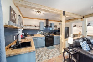 A compact kitchen with a stove, microwave, and cabinets, leading to a dining area with a sofa and a coffee table.