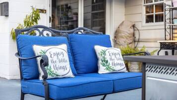 A blue outdoor sofa with two cushions, one with a floral design and the other with a motivational quote.