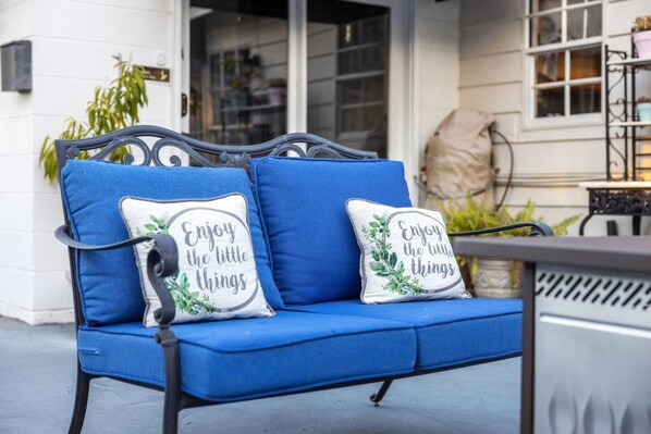 A blue outdoor sofa with two cushions, one with a floral design and the other with a motivational quote.