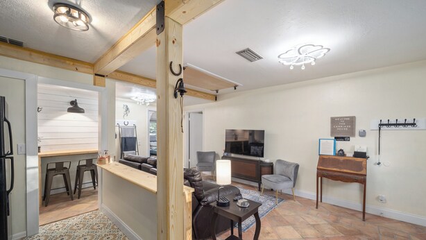 A modern living room with a sofa, TV, and a wooden coffee table. There is a kitchen area with a bar and stools.