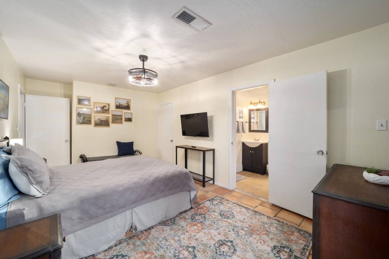 A bedroom with a bed, a television, a desk, and a bathroom visible through an open door.