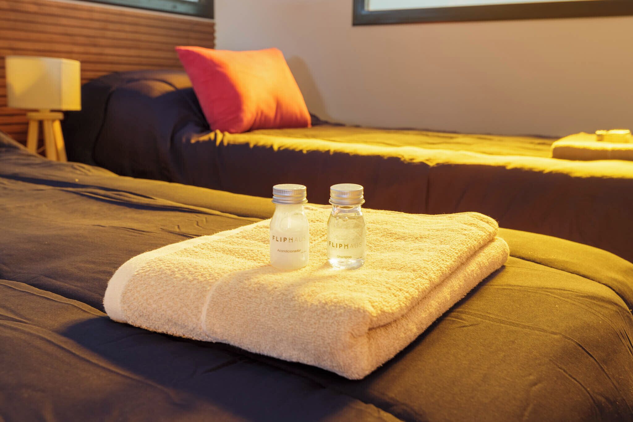 Una cama bien hecha con una toalla doblada y dos botellas de productos FlipHair encima.