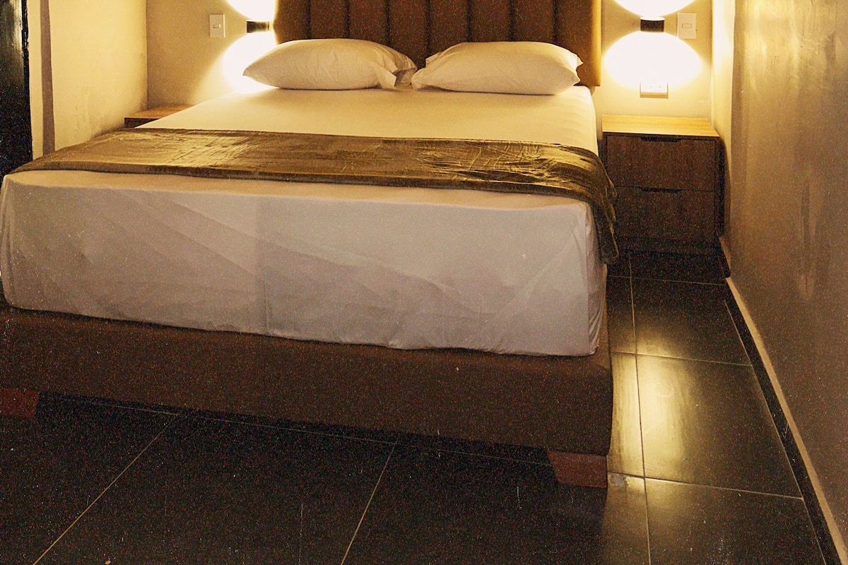 A single bed with a wooden headboard, two bedside lamps, and an air conditioning unit on the wall.