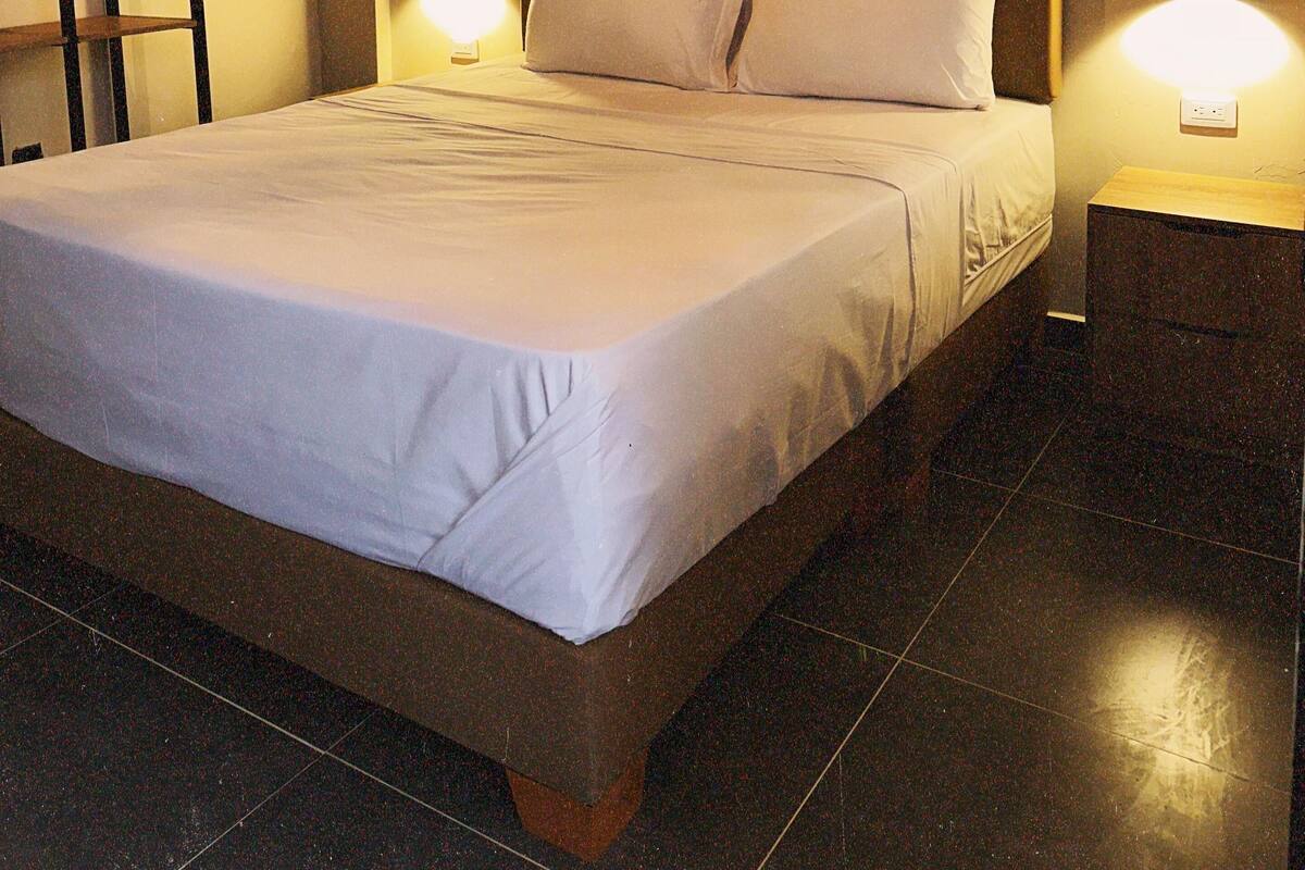 Ein ordentlich bezogenes Bett mit weißen Leinen, einem Holzkopfstück und zwei Nachttischlampen.